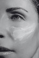 Primer plano en blanco y negro del rostro de una mujer con crema facial hidratante aplicada sobre la mejilla, mostrando su textura.