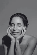 Retrato en blanco y negro de una mujer con los ojos cerrados y las manos sobre el rostro, transmitiendo bienestar y cuidado facial.