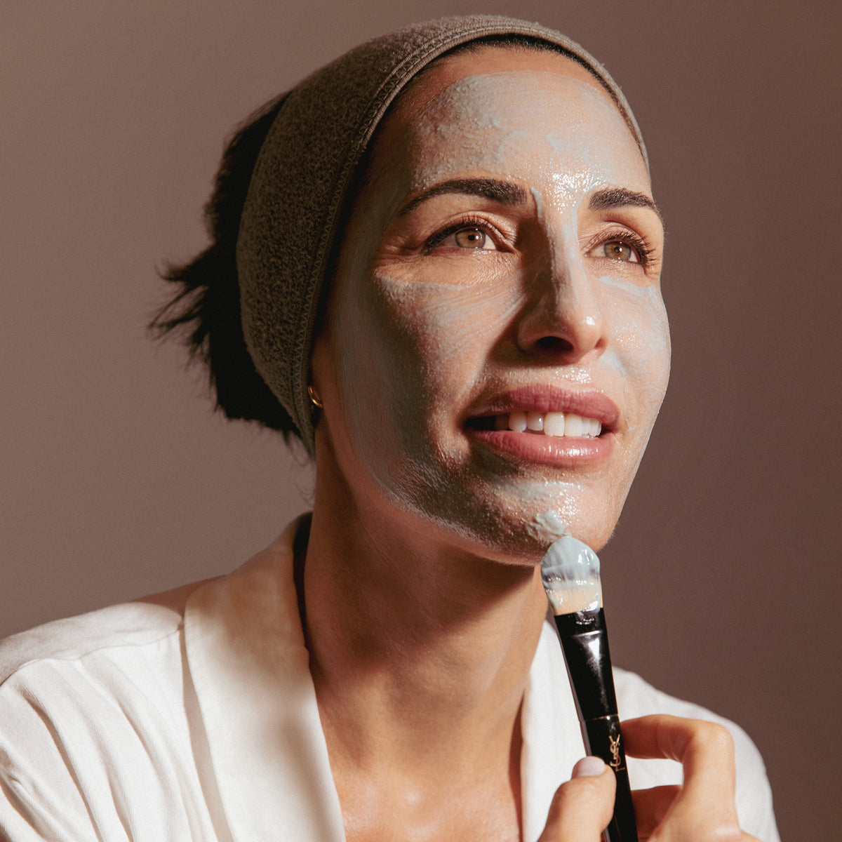 Mujer aplicándose una mascarilla facial con una brocha, como parte de su rutina de cuidado de la piel.