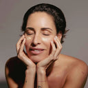 Mujer con los ojos cerrados aplicándose crema en el contorno de ojos con las yemas de los dedos, durante su rutina de cuidado facial.